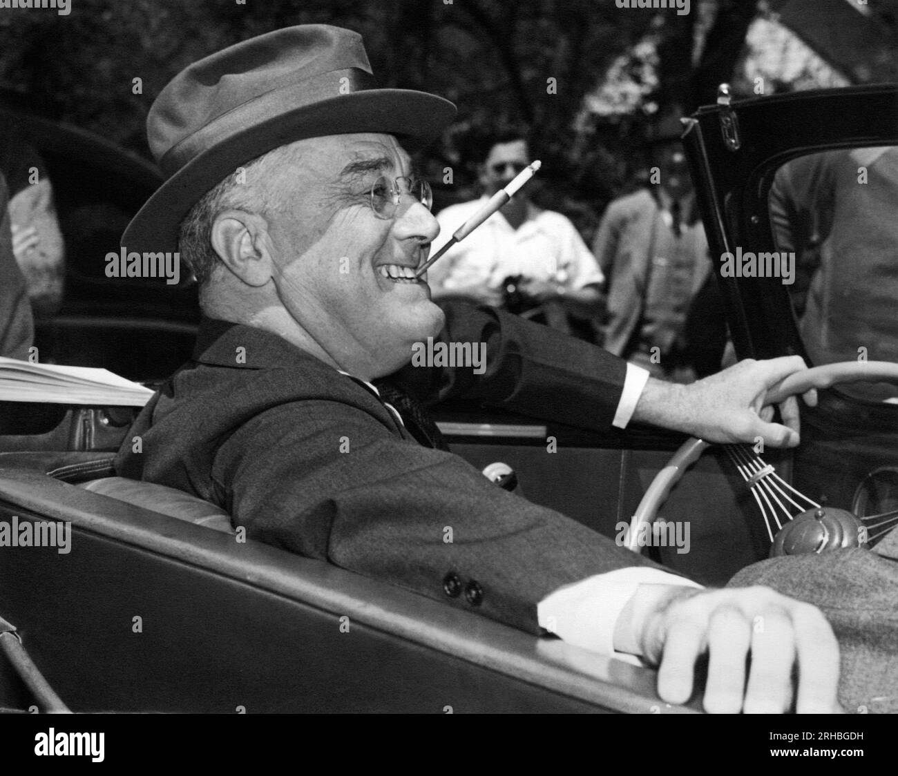 Warm Springs, Georgia:  1939. With a cigarette in a holder clenched in his teeth, a smiling Franklin Delano Roosevelt sits jauntily at the wheel of his convertible. Stock Photo