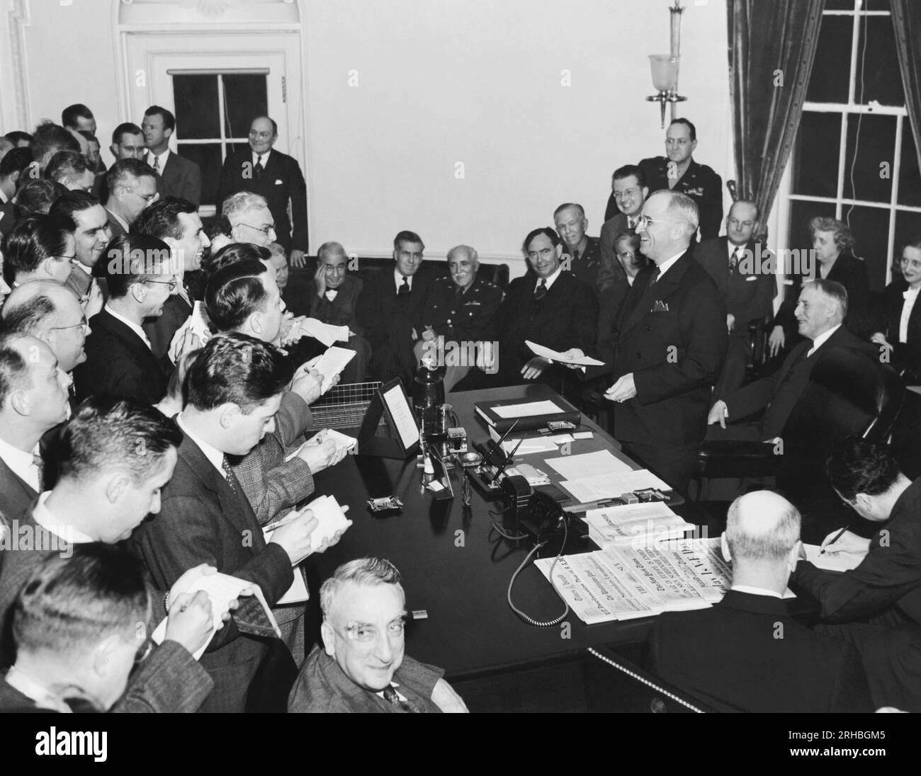Washington, D.C.: May 8, 1945 President Truman as he reads the Victory Proclamation to the press corps, officially announcing the end of the war in Europe. Gathered around are L-R in rear: Elmer Davis (hand to head); Secretary of Commerce Henry A. Wallace; Major General Philip Fleming; Rep. Joseph Martin; General of the Army George C. Marshall; J. Leonard Reinsch; Col. Harry Vaughan; John W. Snyder; Mrs. Truman; Margaret Truman; and Secretary of War Henry L Stimson. In center foreground looking at camera is Fred m. Vinson. Stock Photo