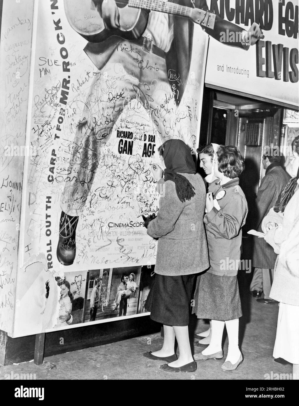 New York, New York:  1956 Teenage girls add to grafitti on the bottom of an Elvis Presley movie poster. Stock Photo