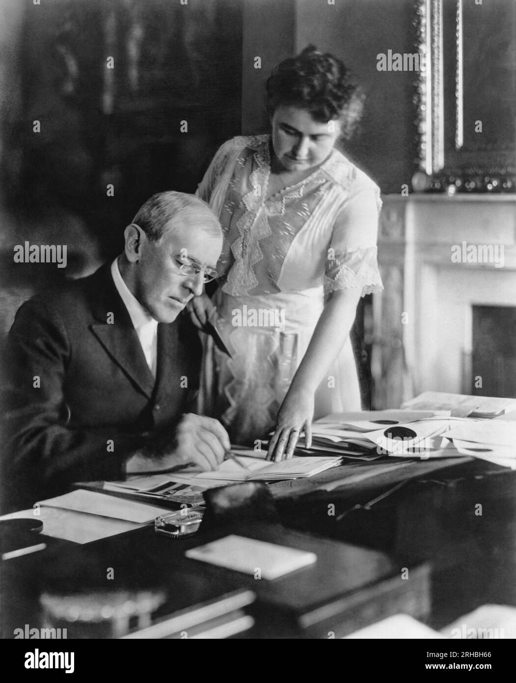 Washington, D.C.:   June, 1920 First Lady Edith Wilson assists President Woodrow Wilson at his desk in the White House. Stock Photo