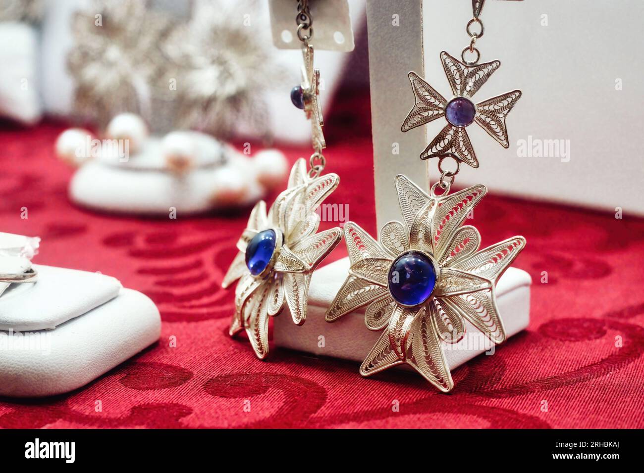 Close up of silver filigree jewellery Earrings in the shape of the Maltese cross with polished shiny blue sapphire gemstones inset in the middle Stock Photo Alamy