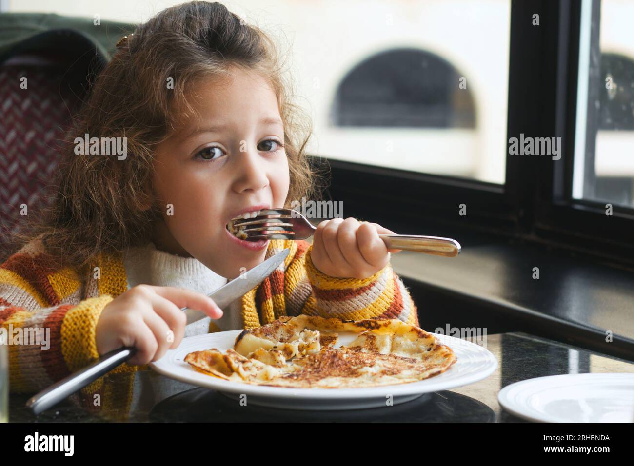 A young white Caucasian girl eating a breakfast pancake with a knife and fork Stock Photo