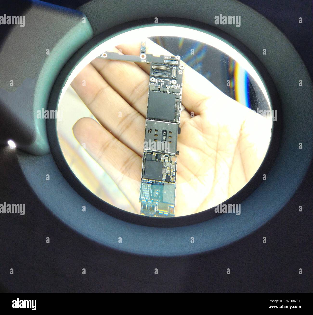 technician using magnifying glass smartphone motherboard Stock Photo