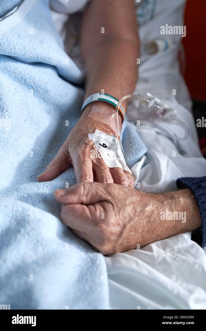 High angle of crop anonymous elderly man holding hand of sick woman