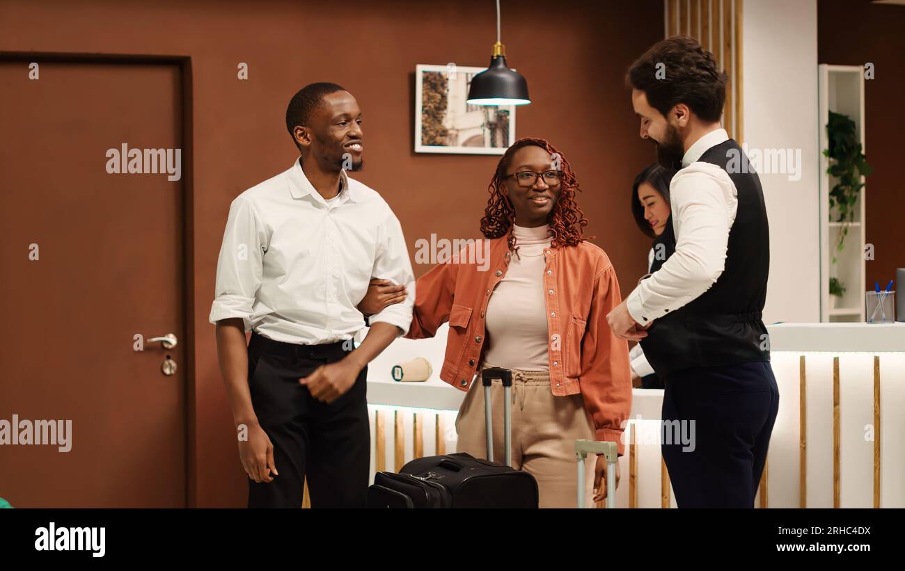 Happy guests tipping helpful porter employee carrying their baggage to