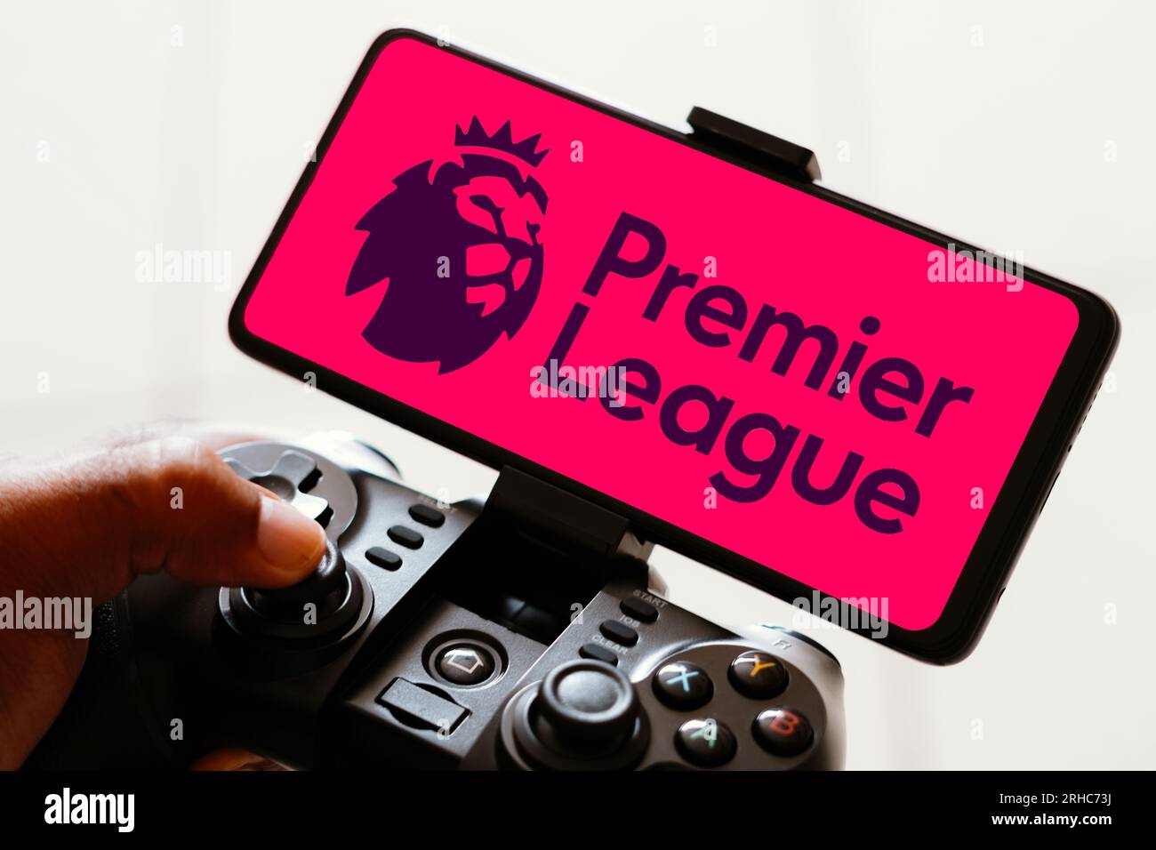 In this photo illustration, the Premier League logo is displayed on a smartphone screen as a person plays on a gaming joystick. Stock Photo