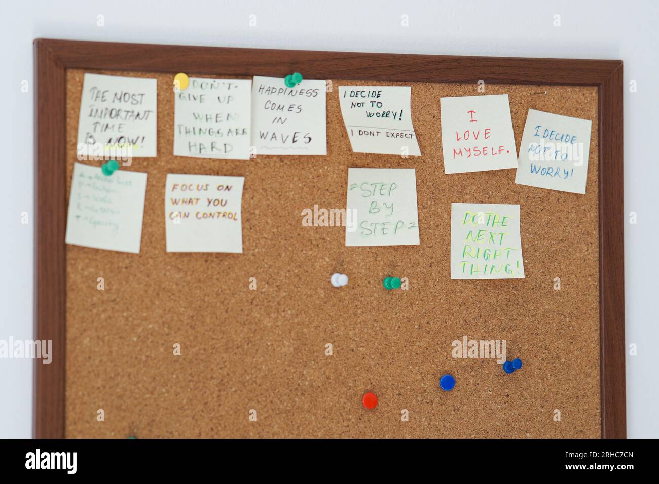 Cork board with stick notes with motivational sentences on them on a white wall. Motivational