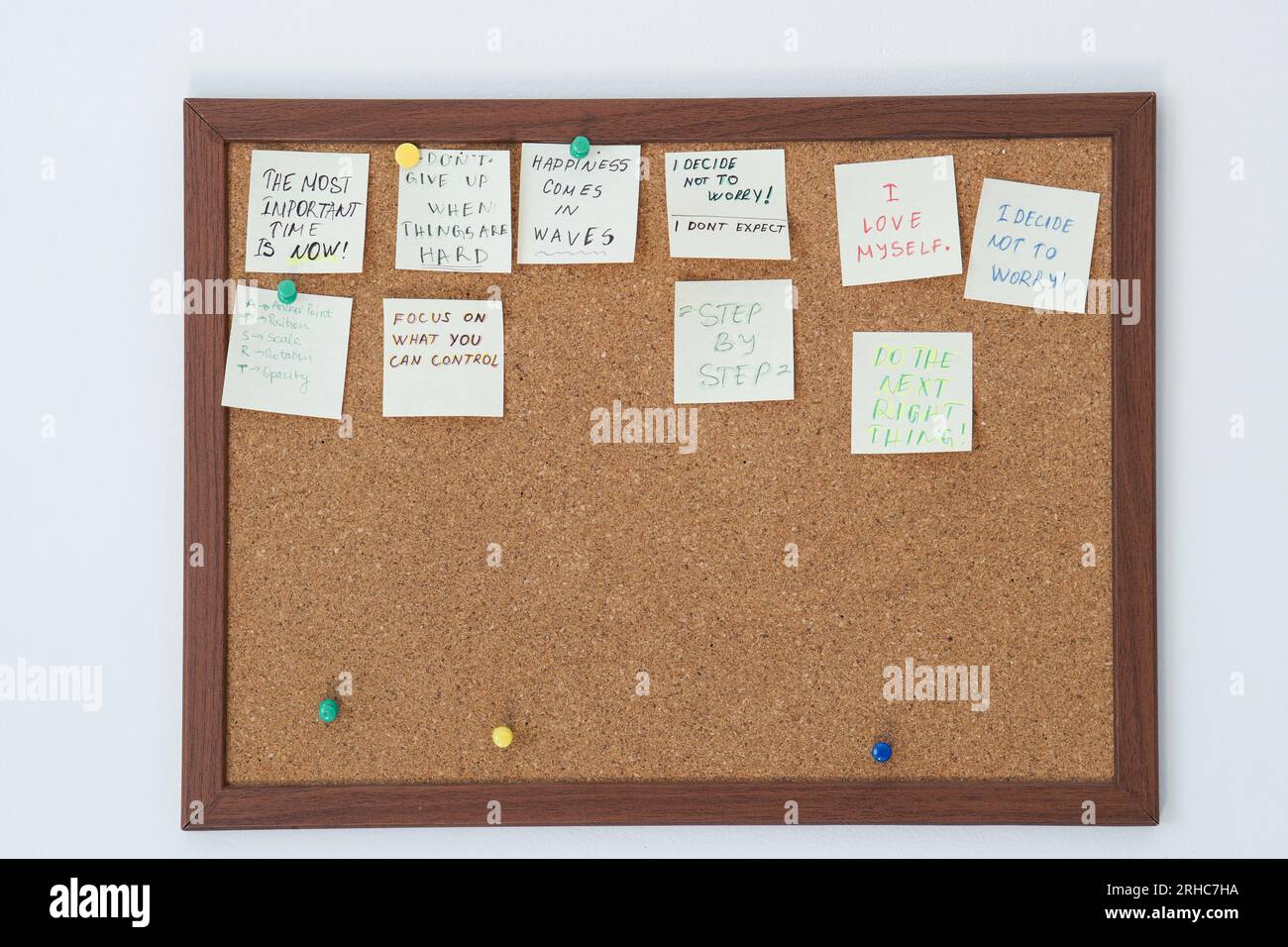Cork board with stick notes with motivational sentences on them on a white wall. Motivational quotes written on stick notes pinned on cork board Stock Photo