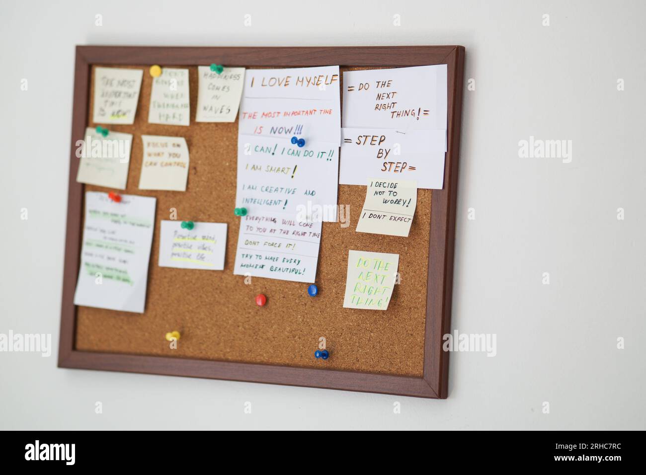 Cork board with stick notes with motivational sentences on them on a white wall. Motivational quotes written on stick notes pinned on cork board Stock Photo