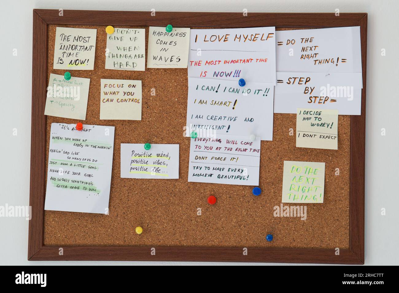 Cork board with stick notes with motivational sentences on them on a white wall. Motivational
