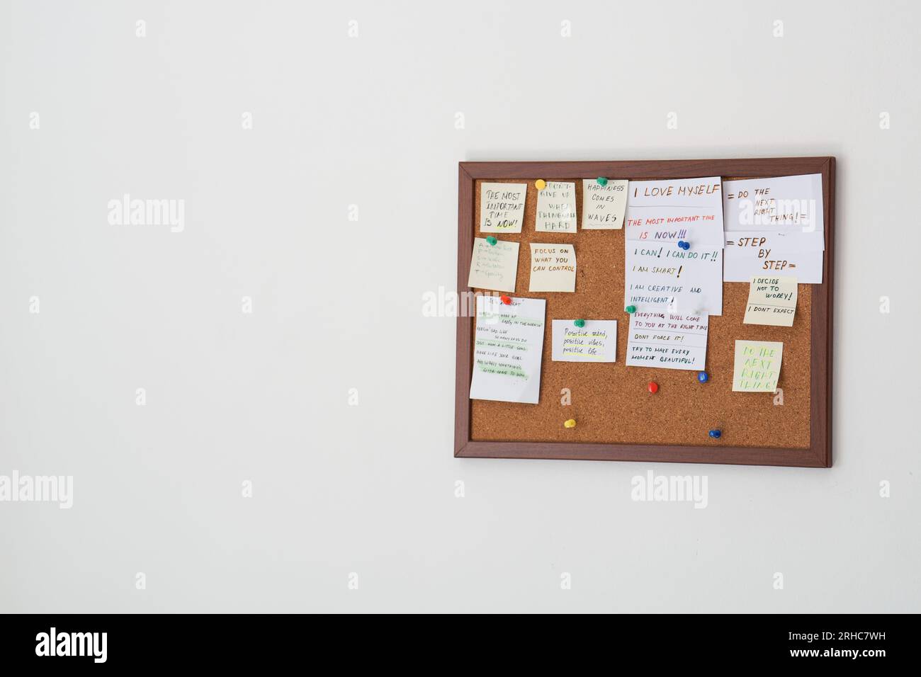 Cork board with stick notes with motivational sentences on them on a white wall. Motivational