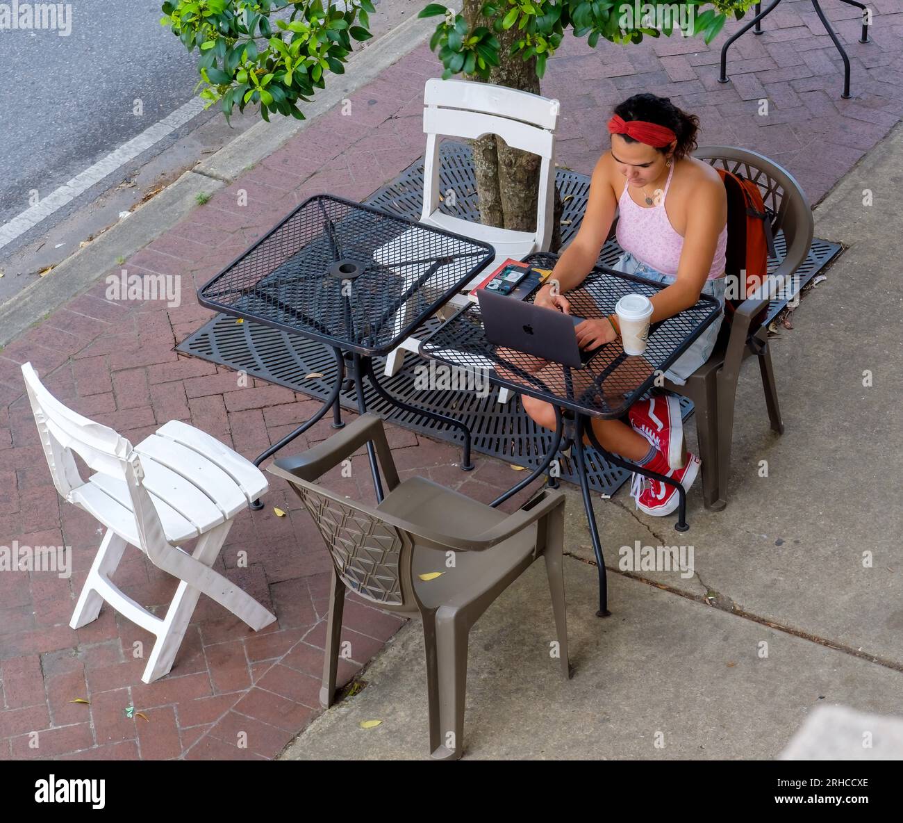 NEW ORLEANS, LA, USA - APRIL 2, 2023: Overhead photo of young woman working on her laptop computer at an outdoor table of the Rue de la Course Cafe Stock Photo