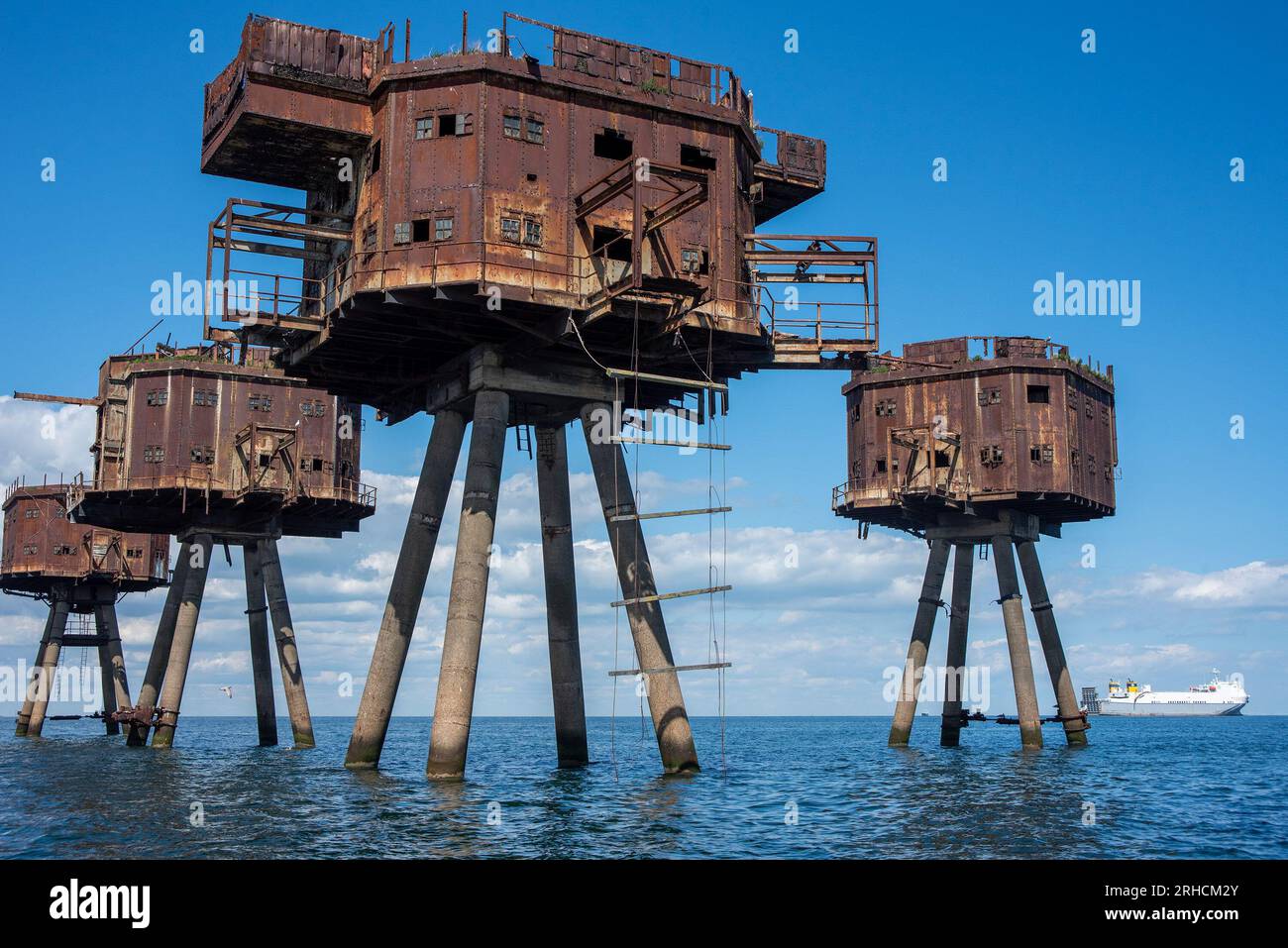 The Maunsell Forts seen with very serious structural defects and many of their parts fallen into the sea. Nowadays only the seagulls nest in them. A ferry boat is visible at the distance as this water is not safe for boating. The Maunsell Forts are armed towers built at the Thames and the Mersey Estuaries during the Second World War to defend the United Kingdom. They have been built 1942 - 1943 for anti-aircraft defense and to report to London about the German aircraft. They are all named after the designer Guy Maunsell. Stock Photo