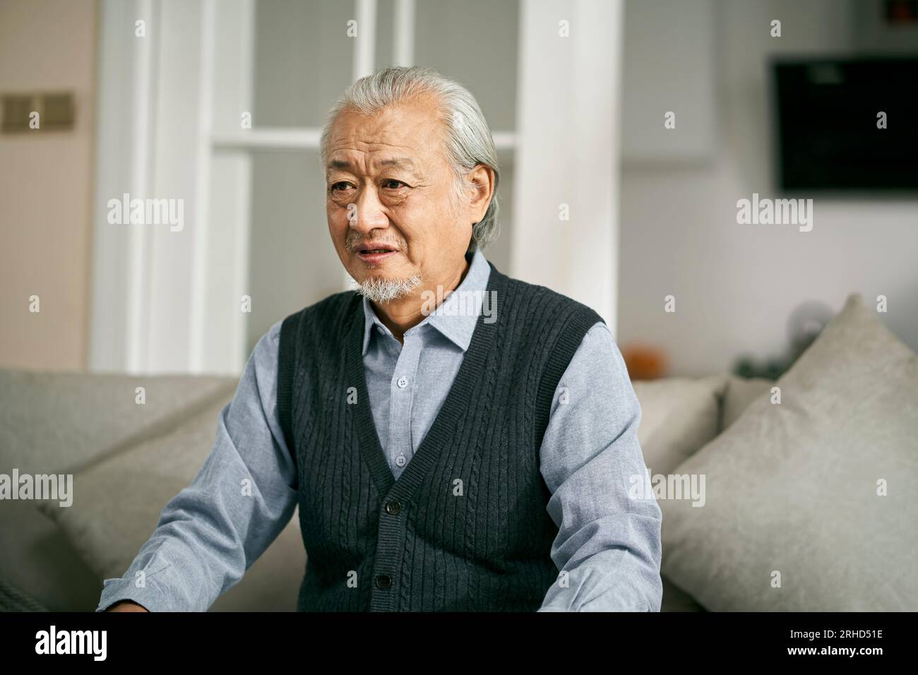 sad senior asian man sitting on couch in living room at home weeping Stock Photo