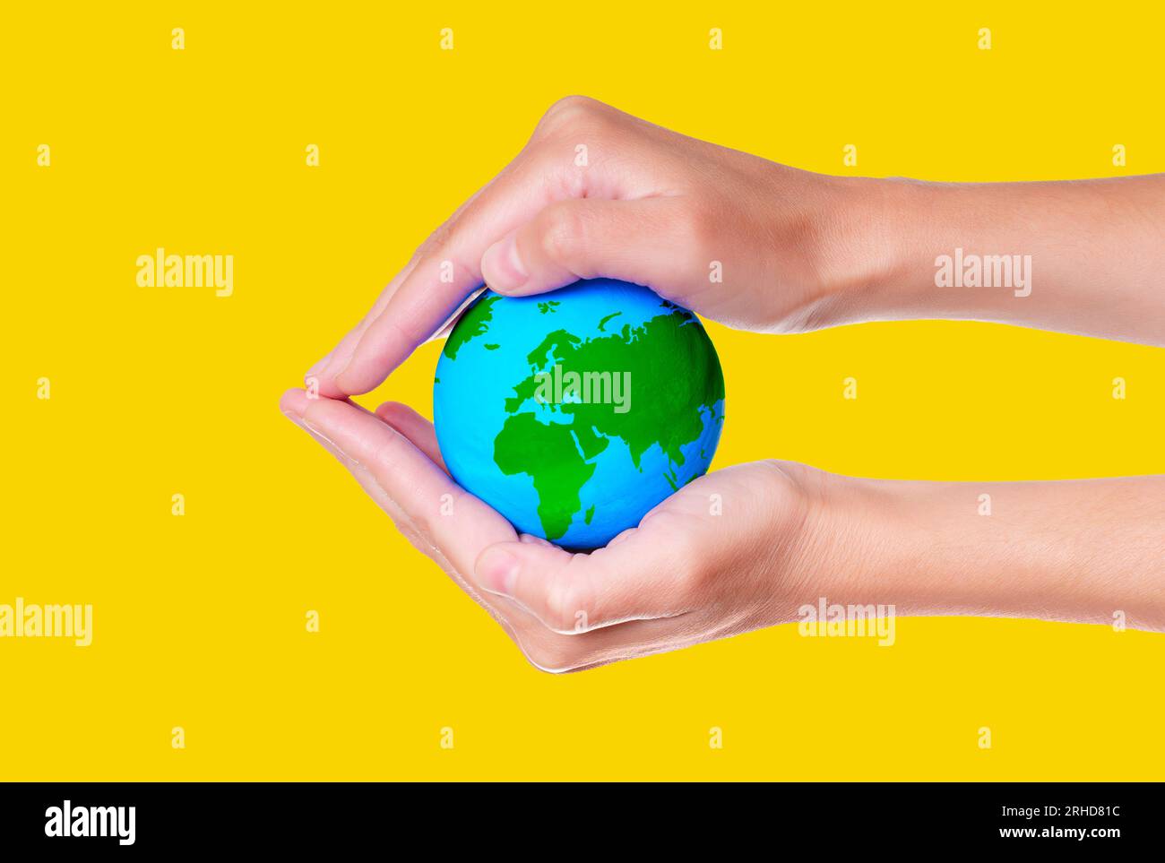 Cupped hands cradle a miniature green and blue globe isolated on yellow ...