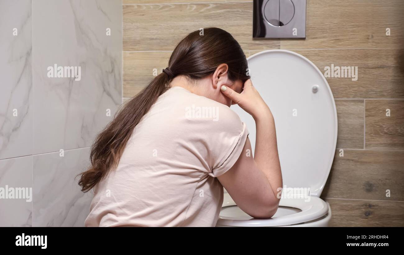 Woman feels nauseous sitting near toilet in bathroom Stock Photo