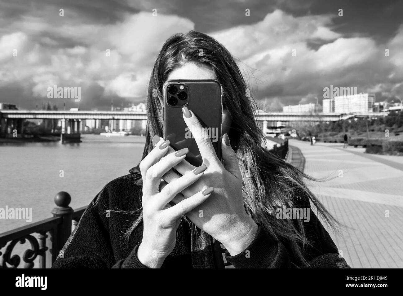 a young woman takes a photo or video on a smartphone covering her face with a smartphone, black and white photo Stock Photo