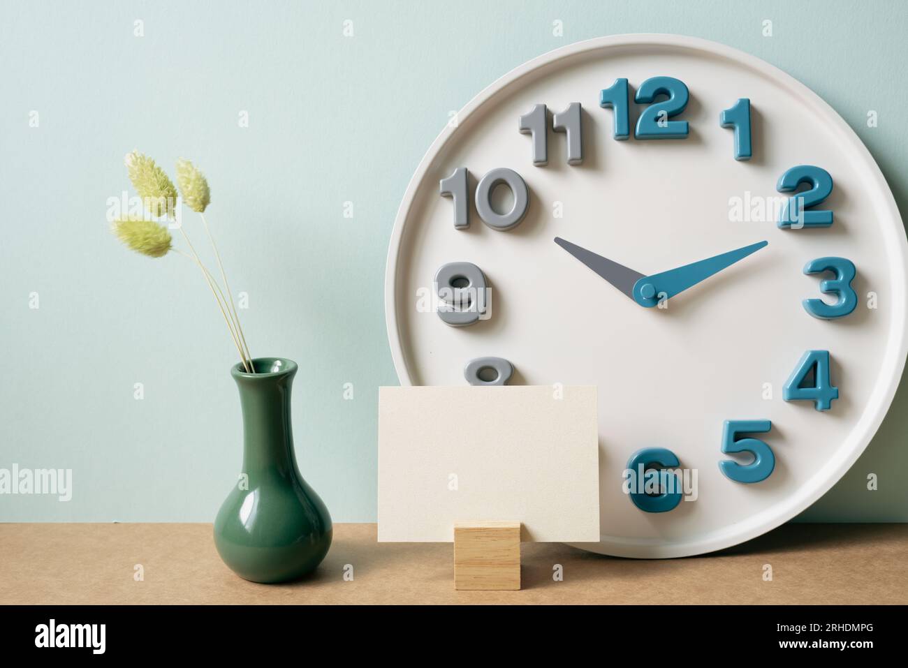 Memo pad holder, clock, vase of dry plant on brown desk. mint wall background. workspace, copy space Stock Photo