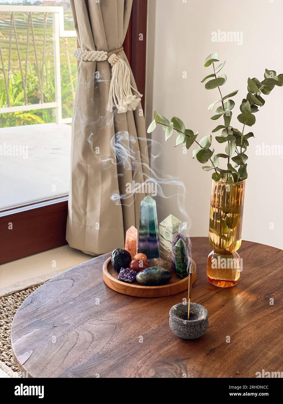 Glass vase with with eucalyptus leaves, various healing crystals and incense stick on the coffee
