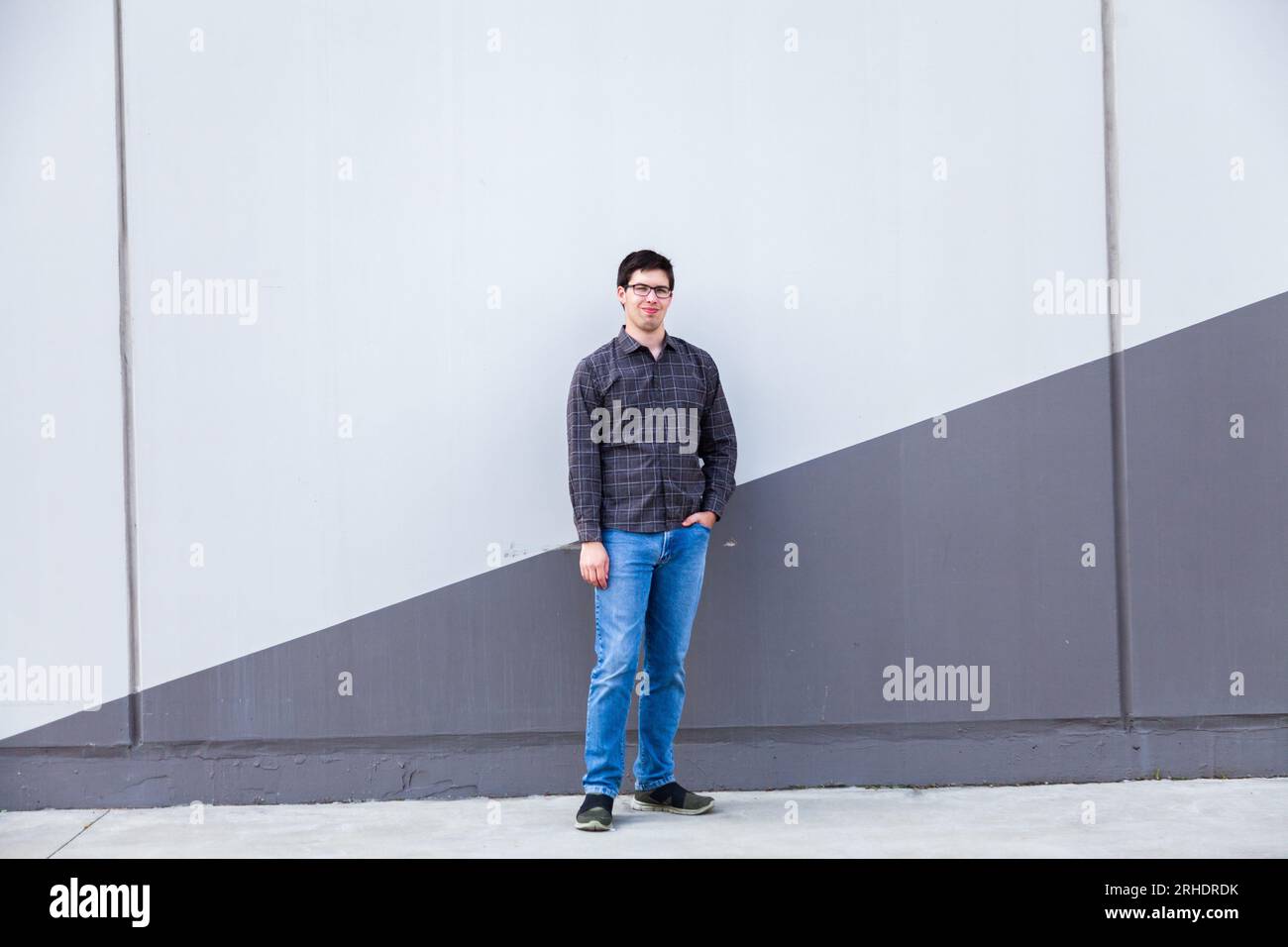 Young man standing in urban area against grey wall with slash down centre in angle Stock Photo