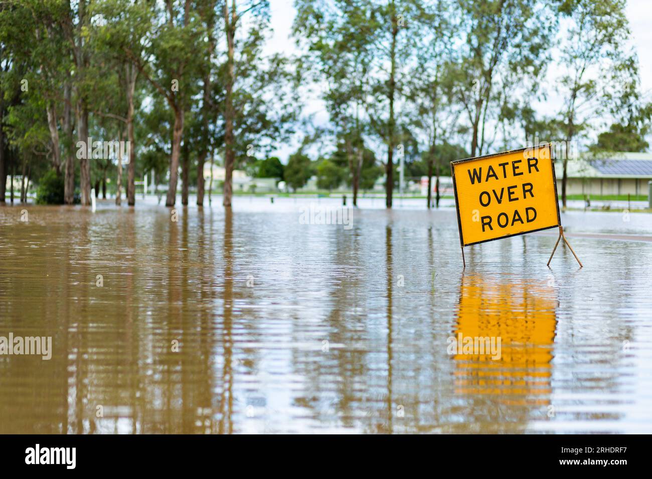 Water over road sign going under floodwaters as flood water rises Stock Photo