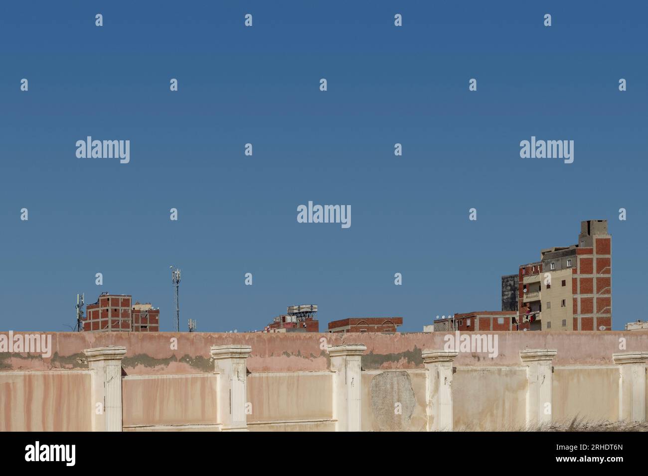 Apartment blocks in Alexandria behind a concrete wall with lots of blue sky, Egypt Stock Photo