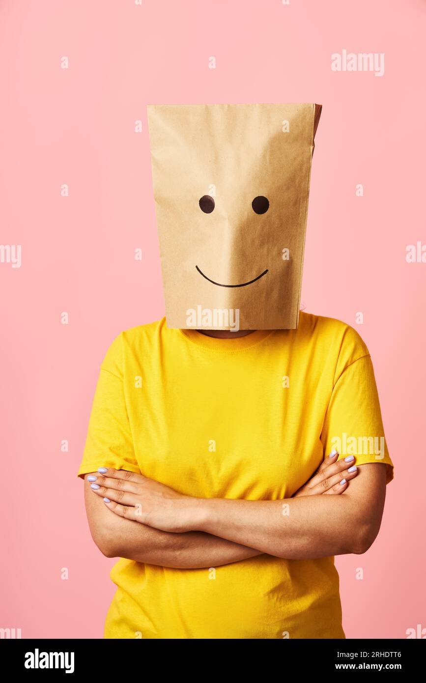 Confident young woman in smiling paper bag on head and crossed arms over pink background. Emotions concept Stock Photo
