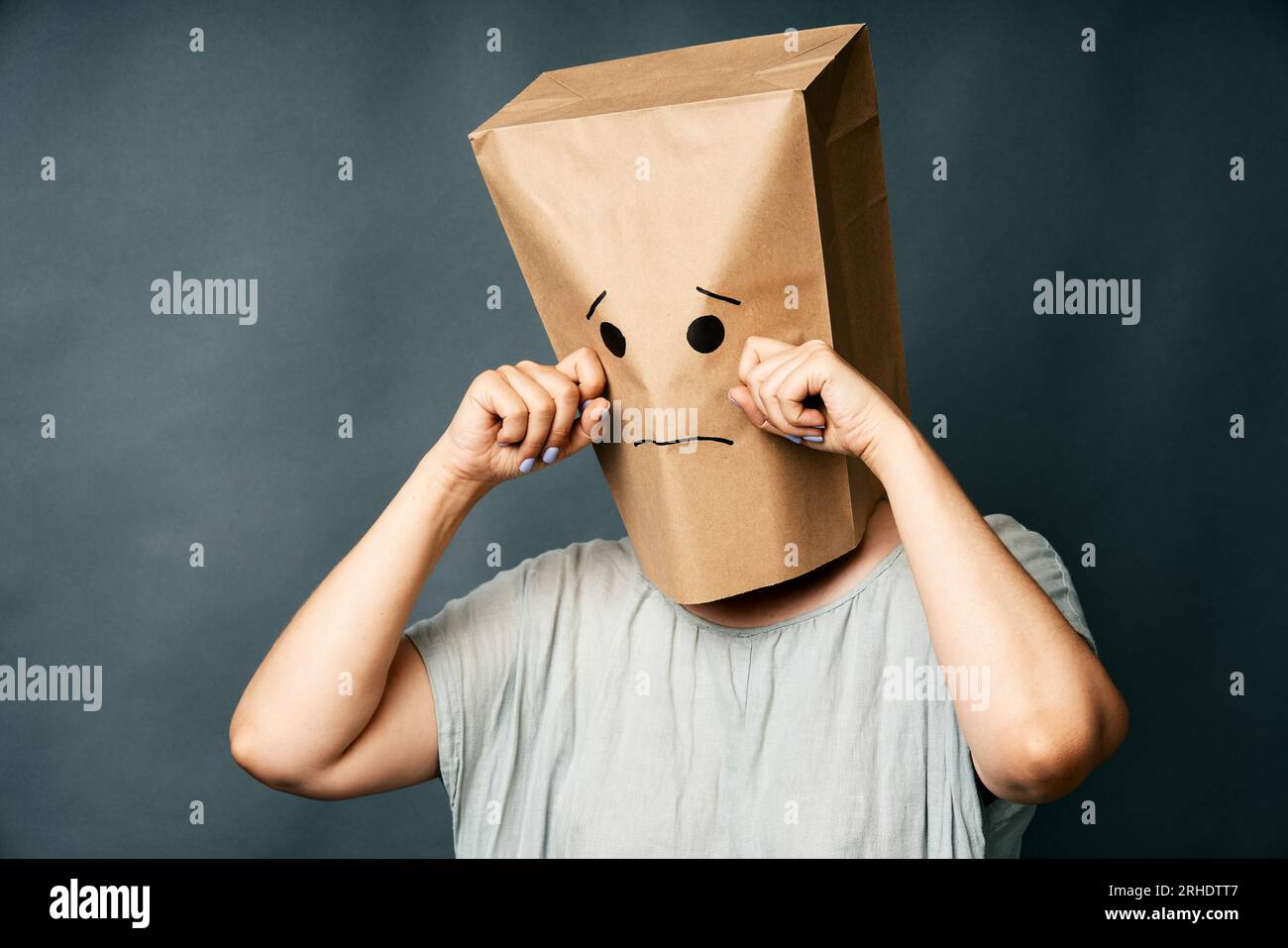 Upset crying woman with a paper bag on head over gray background. Emotion concept Stock Photo
