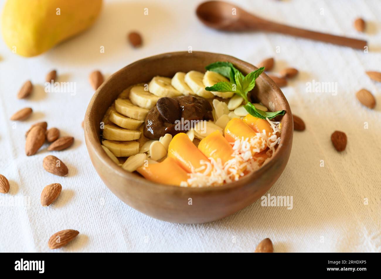 High angle of wooden bowl filled with fresh banana and mango slices almonds and melted chocolate Stock Photo