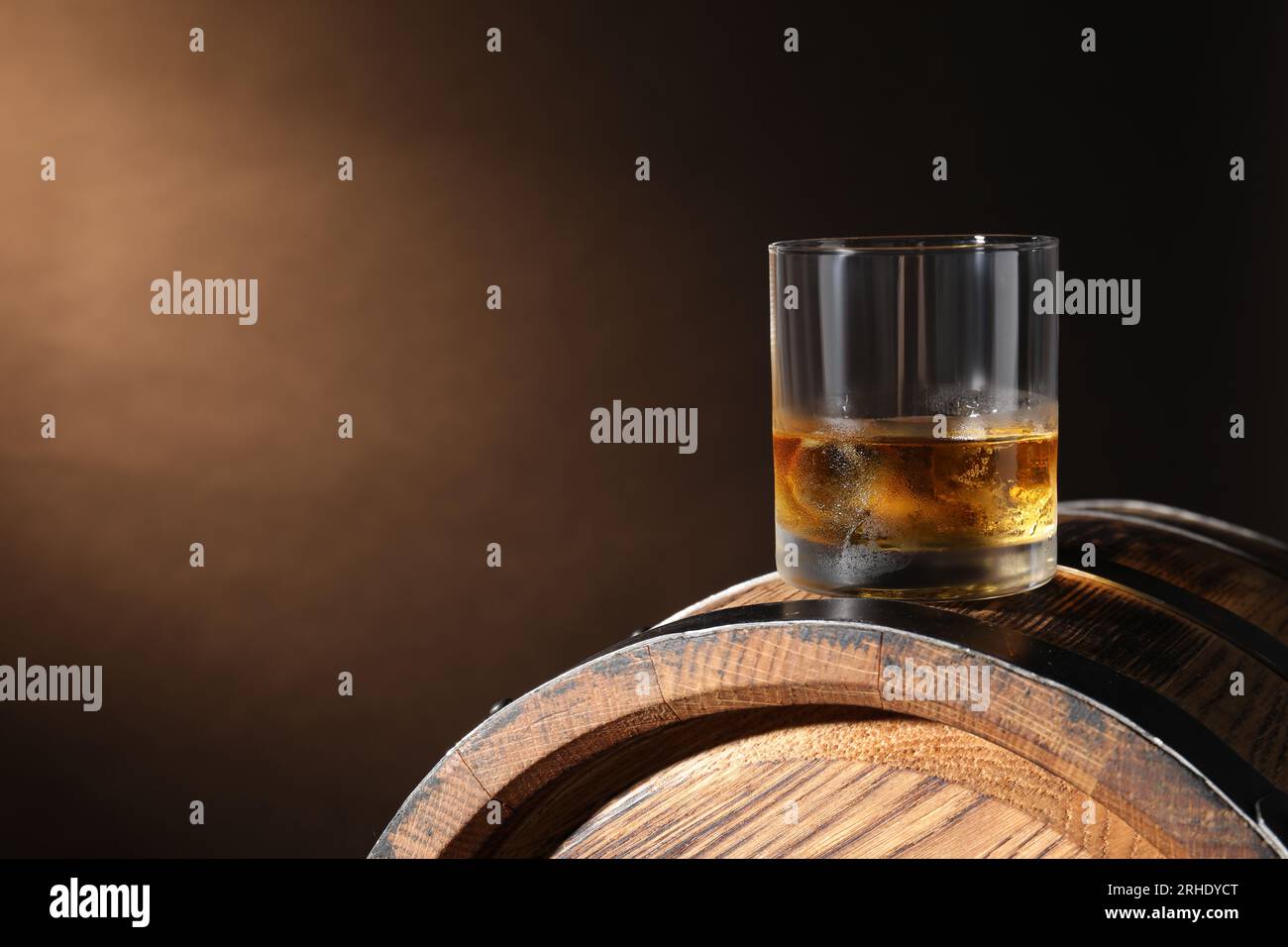 Glass of tasty whiskey on wooden barrel against dark background, space for text Stock Photo