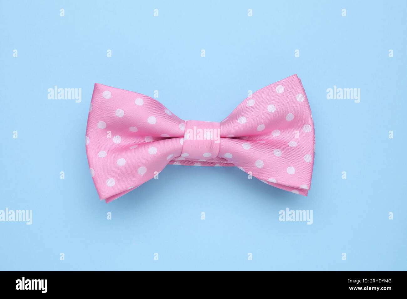 Stylish pink bow tie with polka dot pattern on light blue background, top view Stock Photo