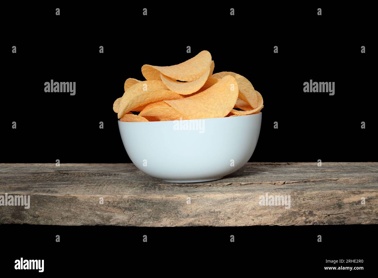 Potato chips bowl standing on old wooden plank, on black background close-up Stock Photo