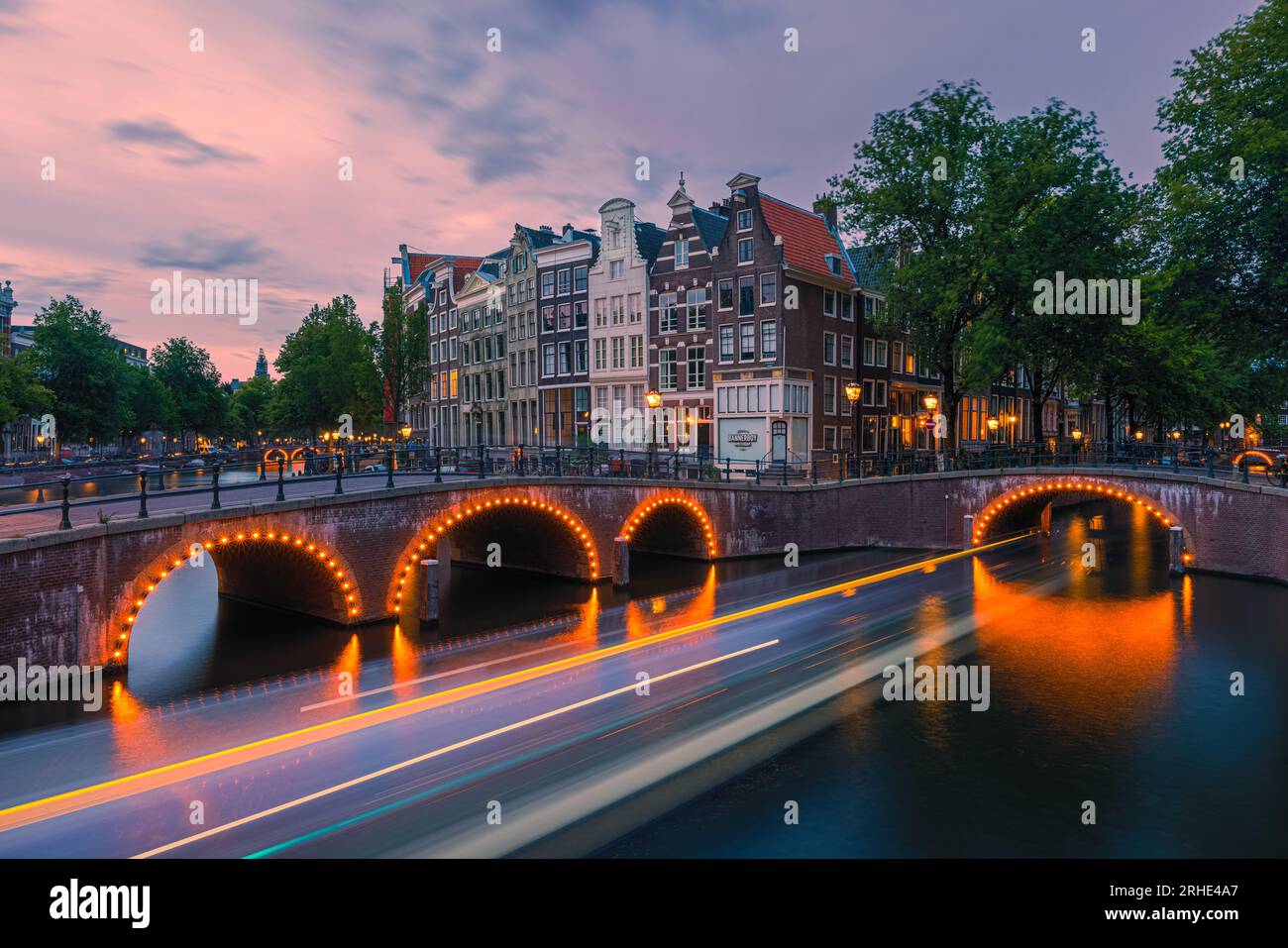 A summer evening with the view on the corner of the Keizersgracht and Leidsegracht witha canalboat is passing by under the bridge in downtown Amsterda Stock Photo