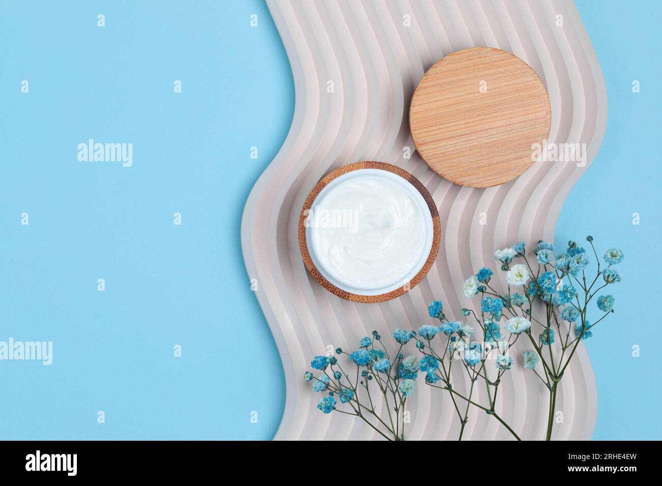 Cosmetic cream jar on concrete decoration wave with field flowers, minimalistic style concept on blue background, top view Stock Photo
