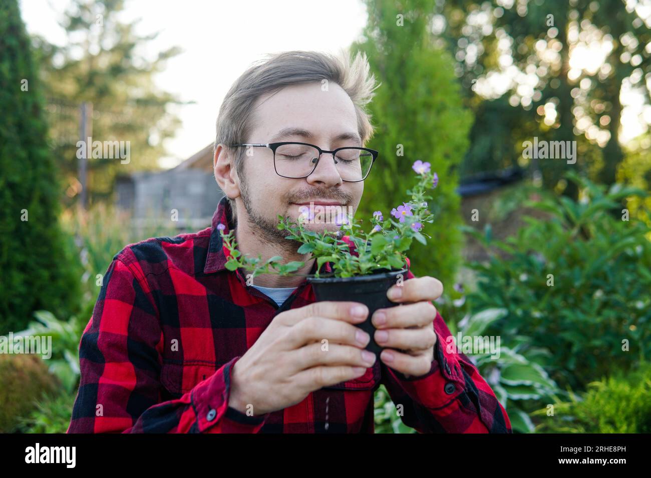 Young man gardener in glasses smelling flowers in pot with eyes closed in greenhouse Stock Photo