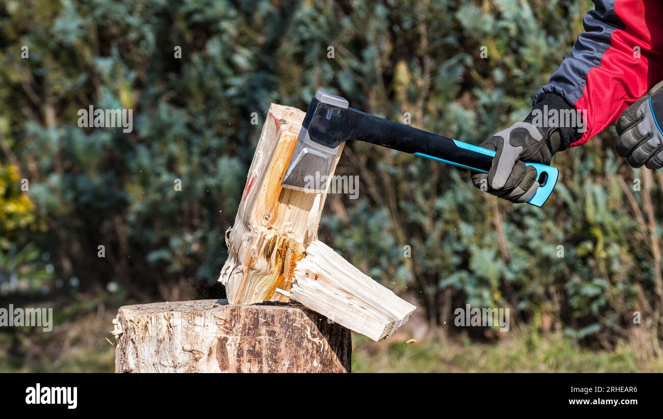 Closeup a sharp axe in human hand when splitting wood log on chopping block. Working man holding modern cutting tool with metal blade and plastic haft. Stock Photo