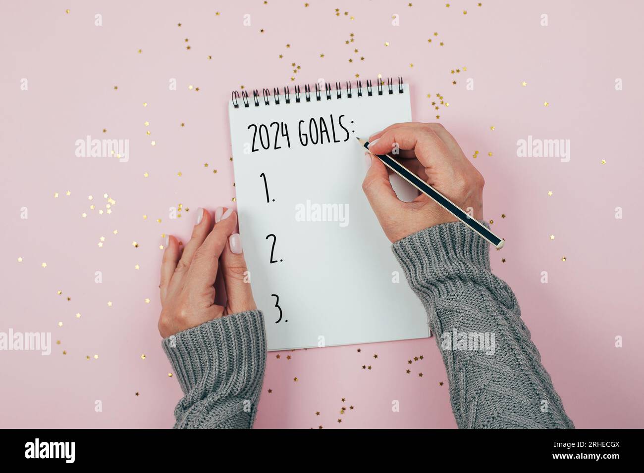 Woman's hand writing list of goals in empty notebook. New Year goals 2024. Top view, flat lay Stock Photo