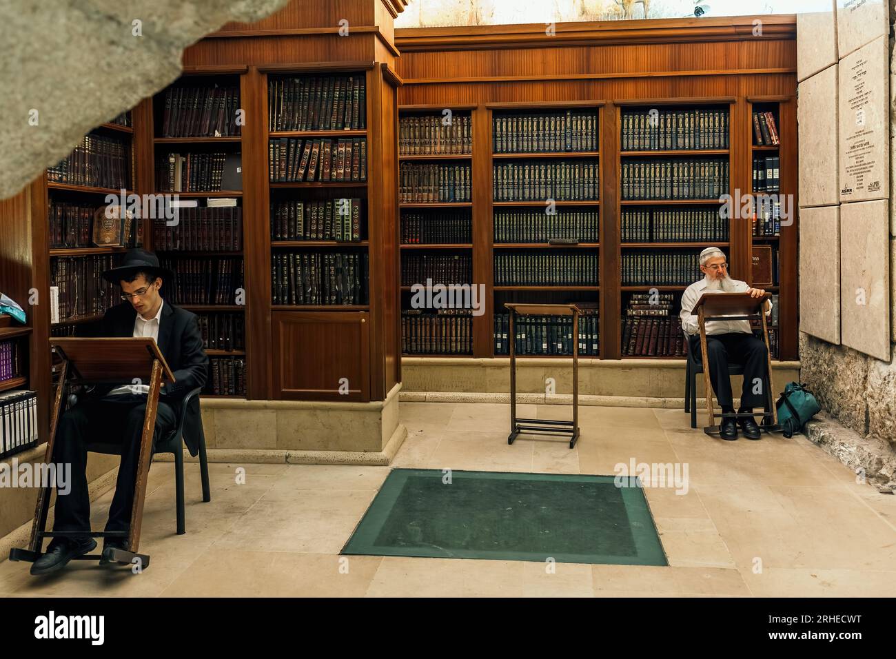 Two religious men sit and pray among bookshelves with holy books inside