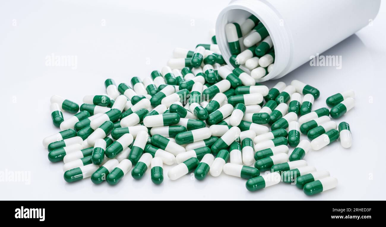 Green and white capsule pills spilled out of a white plastic bottle. Pharmaceutical industry. Prescription drug. Healthcare and medicine. Pharmacy Stock Photo