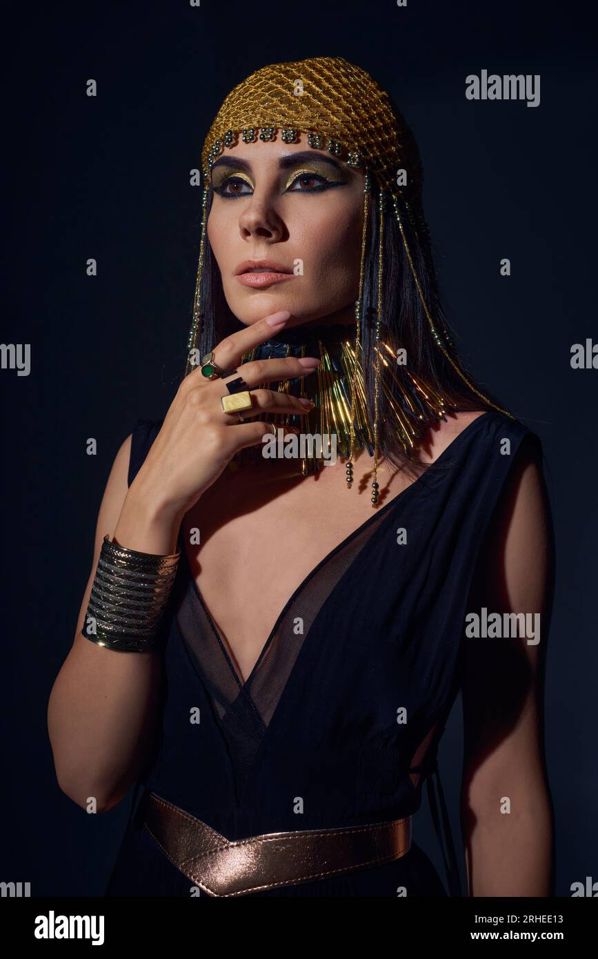 Portrait of woman in egyptian headdress and costume touching chin while