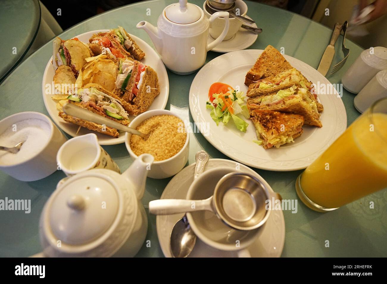 Butter scones with jam and clotted cream served with ham cheese sandwiches and tea pots Stock Photo