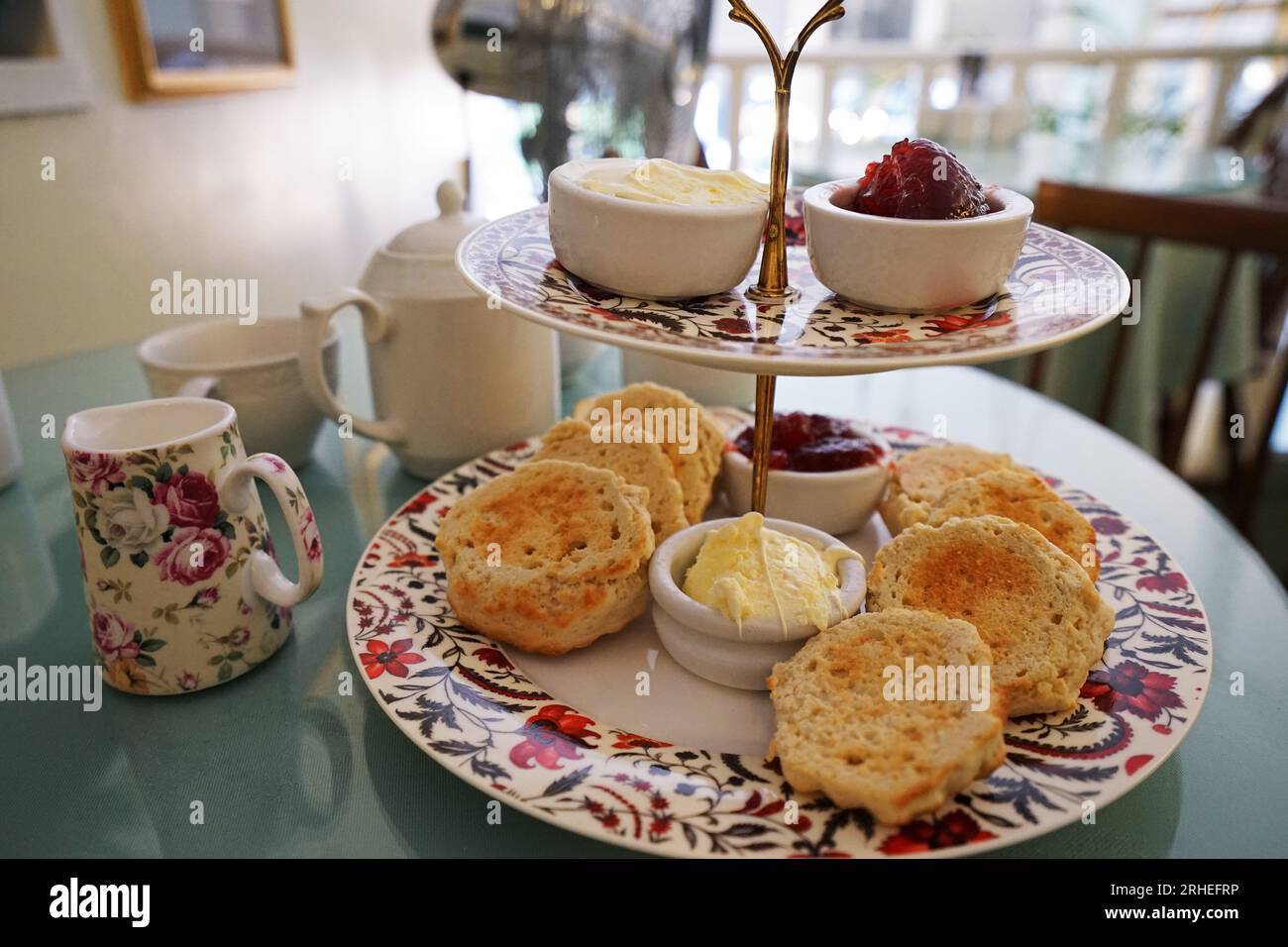 Butter scones with jam and clotted cream served with ham cheese sandwiches and tea pots Stock Photo