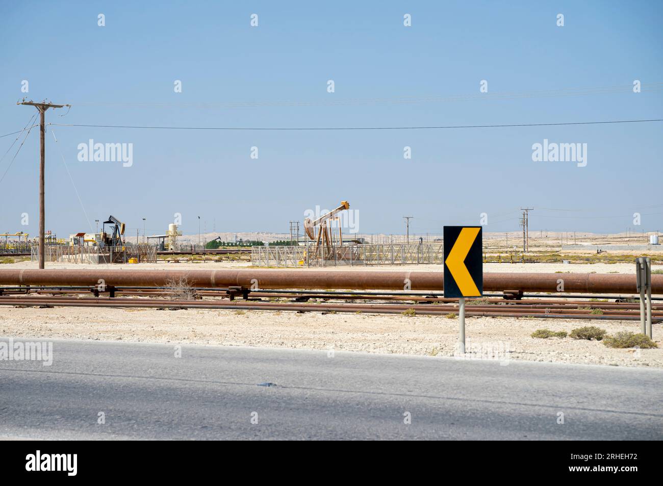 Bahrain oil field infrastructure -  oil pipes, pump jack,oil horse, oil jack, beam pump extracting crude oil from oil wells. Road sign Stock Photo