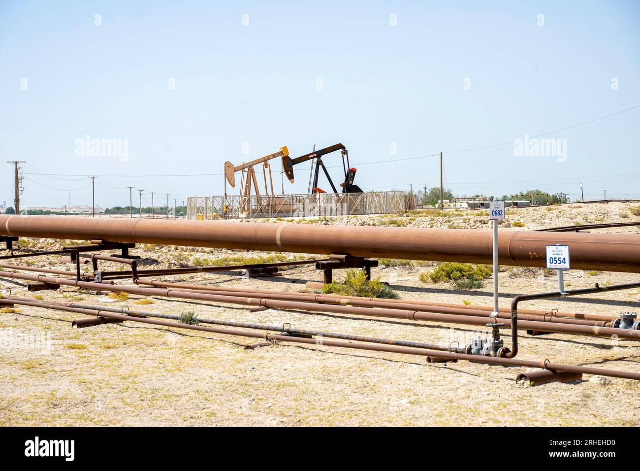 Bahrain oil field infrastructure -  oil pipes, pump jack,oil horse, oil jack, beam pump extracting crude oil from oil well in the Bahrain desert Stock Photo