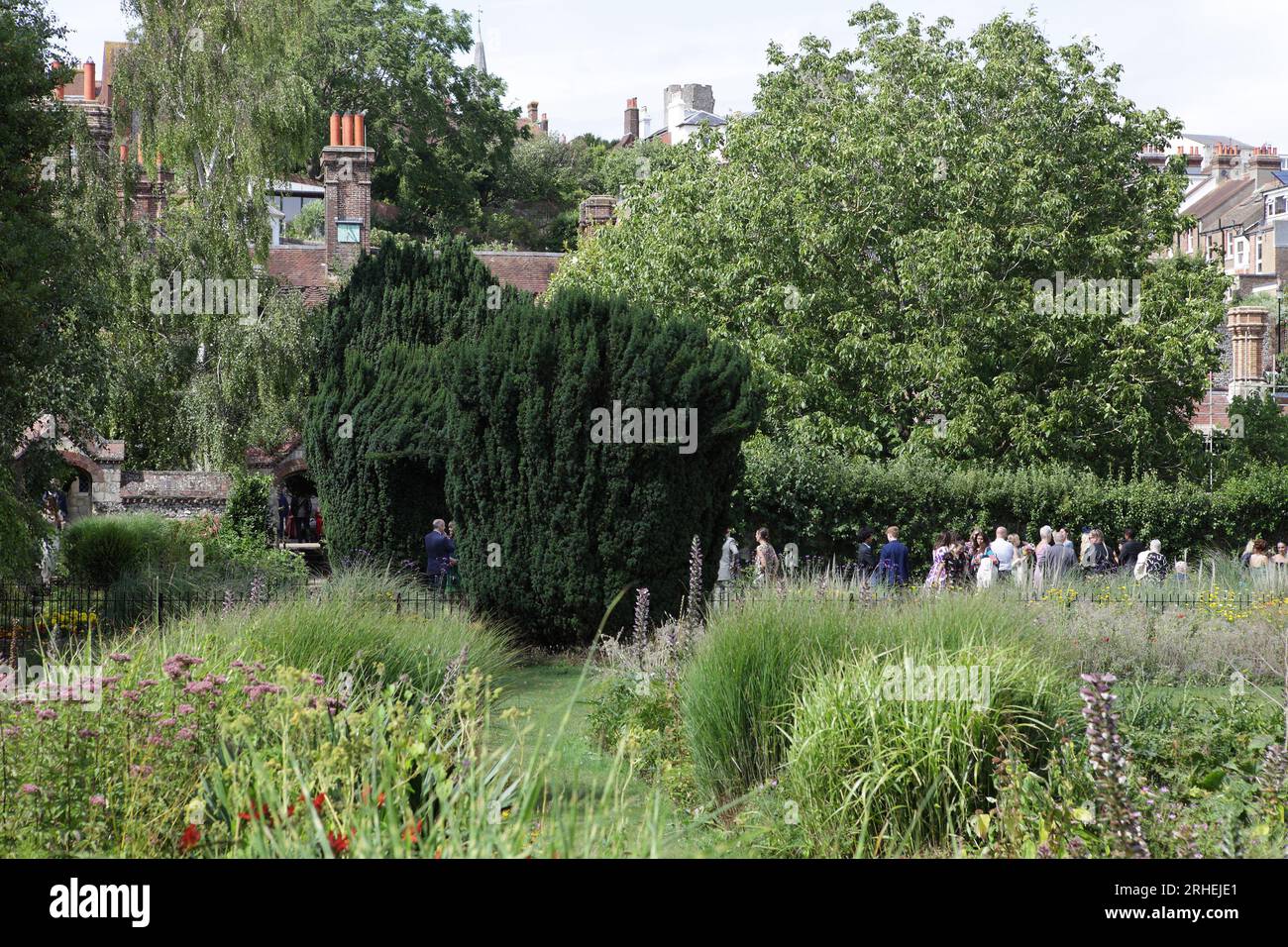 A wedding party congregates in Southover Grange Gardens having first visited the Register Office as seen behind the yew trees. Stock Photo