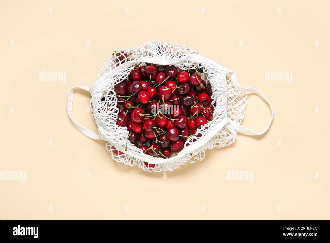 Mesh bag with fresh cherry on beige background Stock Photo