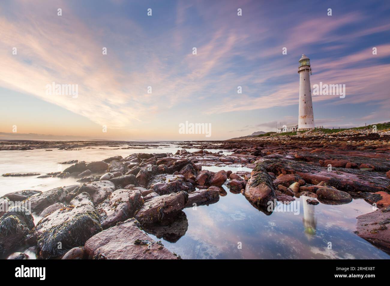 Ocean landscape photograph of the Atlantic ocean Slangkop lighthouse in Kommetjie, South Africa with pink sunset clouds for travelling tourism Stock Photo