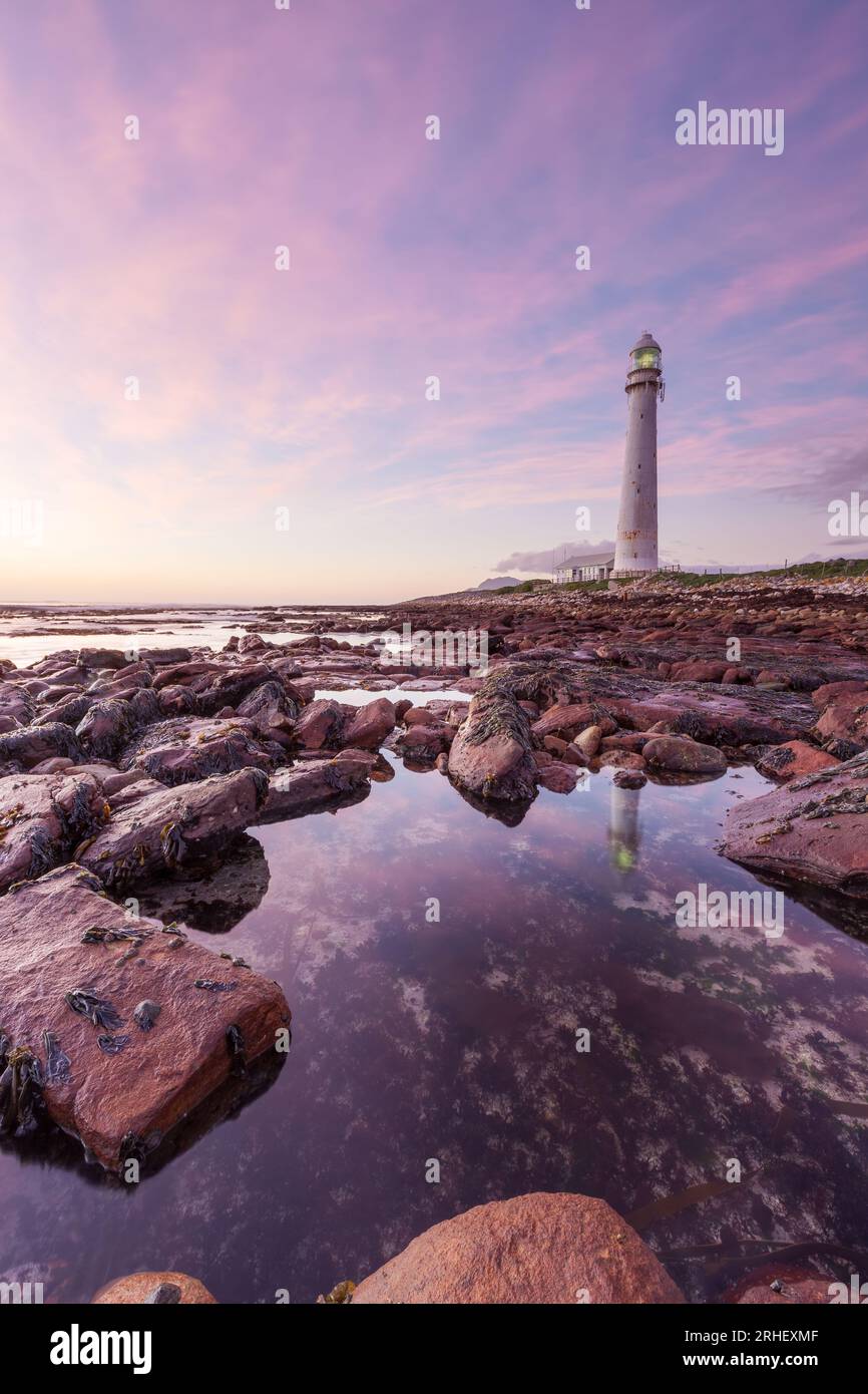 Ocean landscape photograph of the Atlantic ocean Slangkop lighthouse in Kommetjie, South Africa with pink sunset clouds for travelling tourism Stock Photo