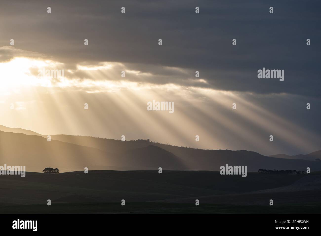 Rays of sun breaking breaking through clouds in the distance at the end of the day over Stock Photo