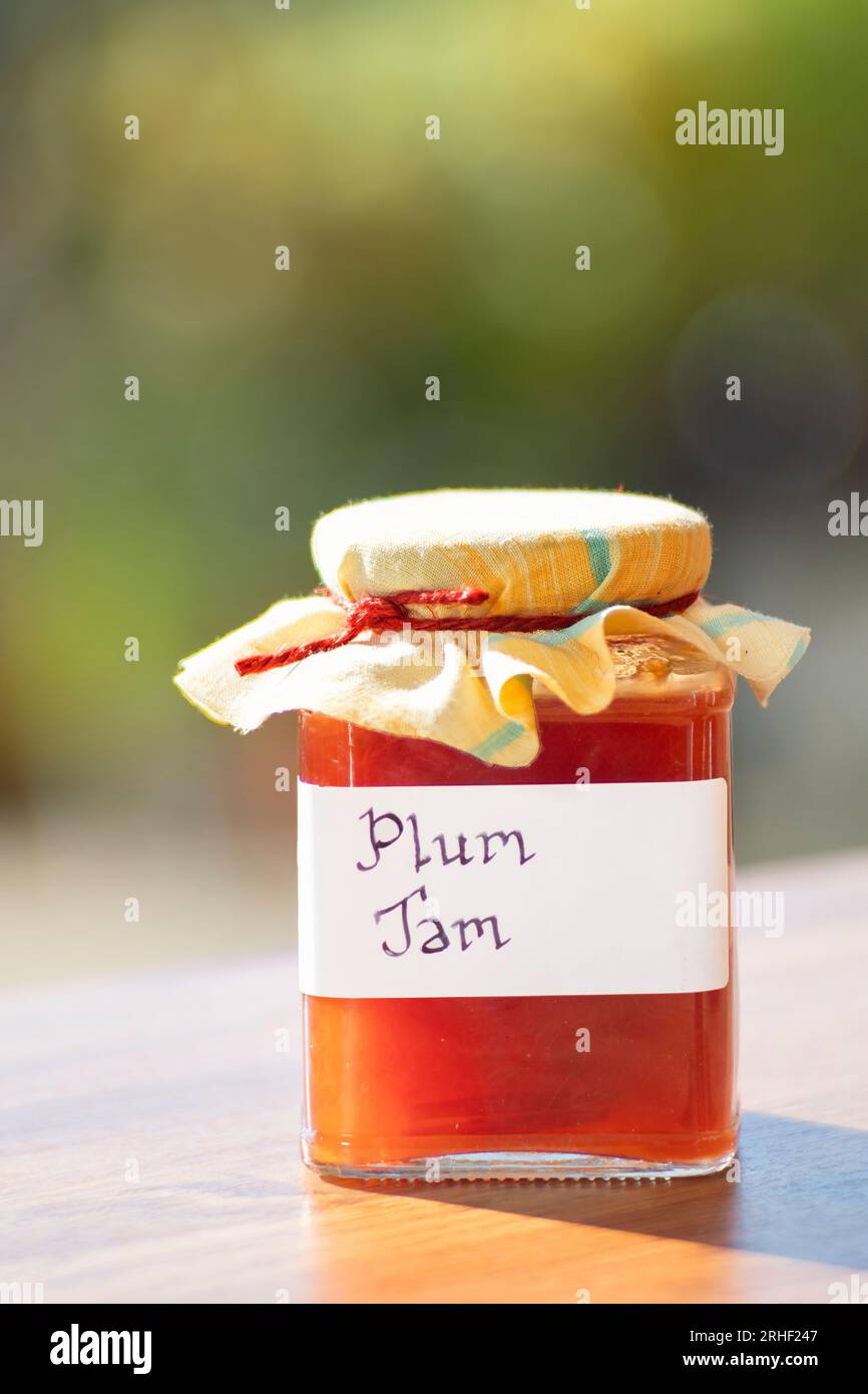 A jar of homemade plum jam. The glass jar has clear handwritten label and the jar have a cloth topping Stock Photo
